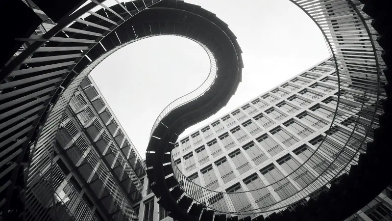 Vue en noir et blanc d’un escalier en colimaçon vu d’en bas, dont la géométrie courbe évoque le mouvement et le changement