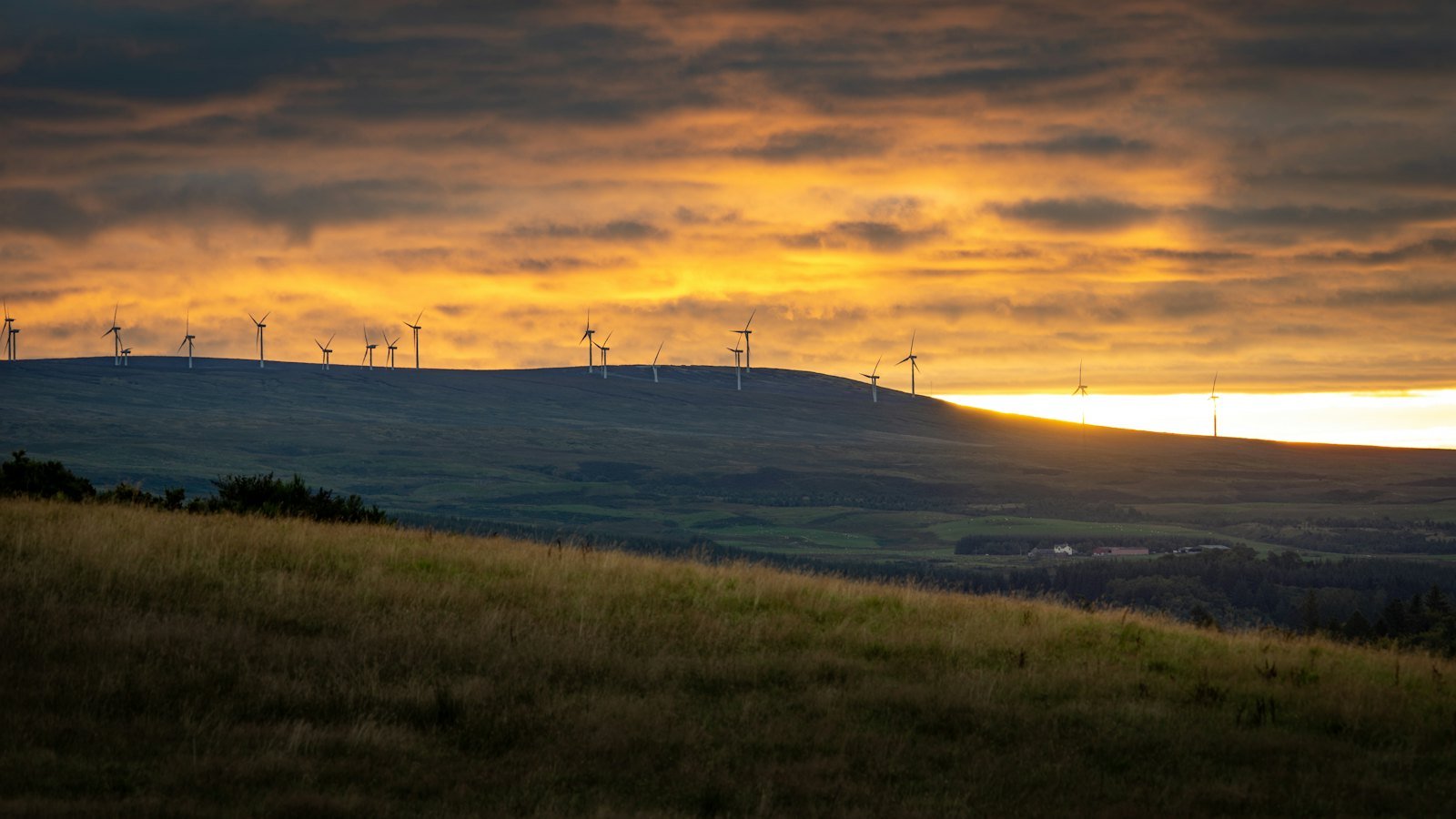 Turbine eoliche su colline verdi sotto un cielo arancione al tramonto