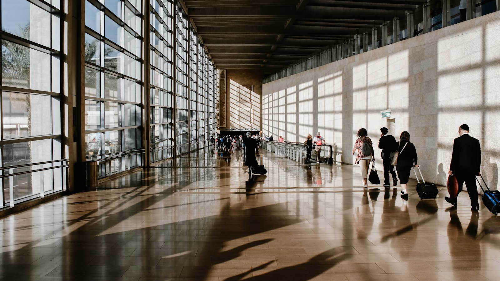 Business travellers walking through a sunlit airport terminal with tall glass windows