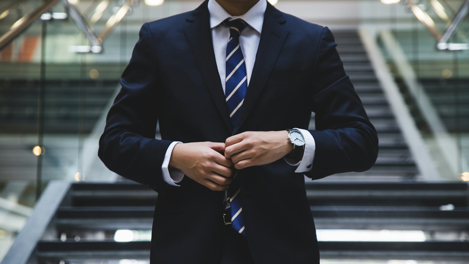 Executive in a dark suit adjusting his cuff on a staircase before an important meeting